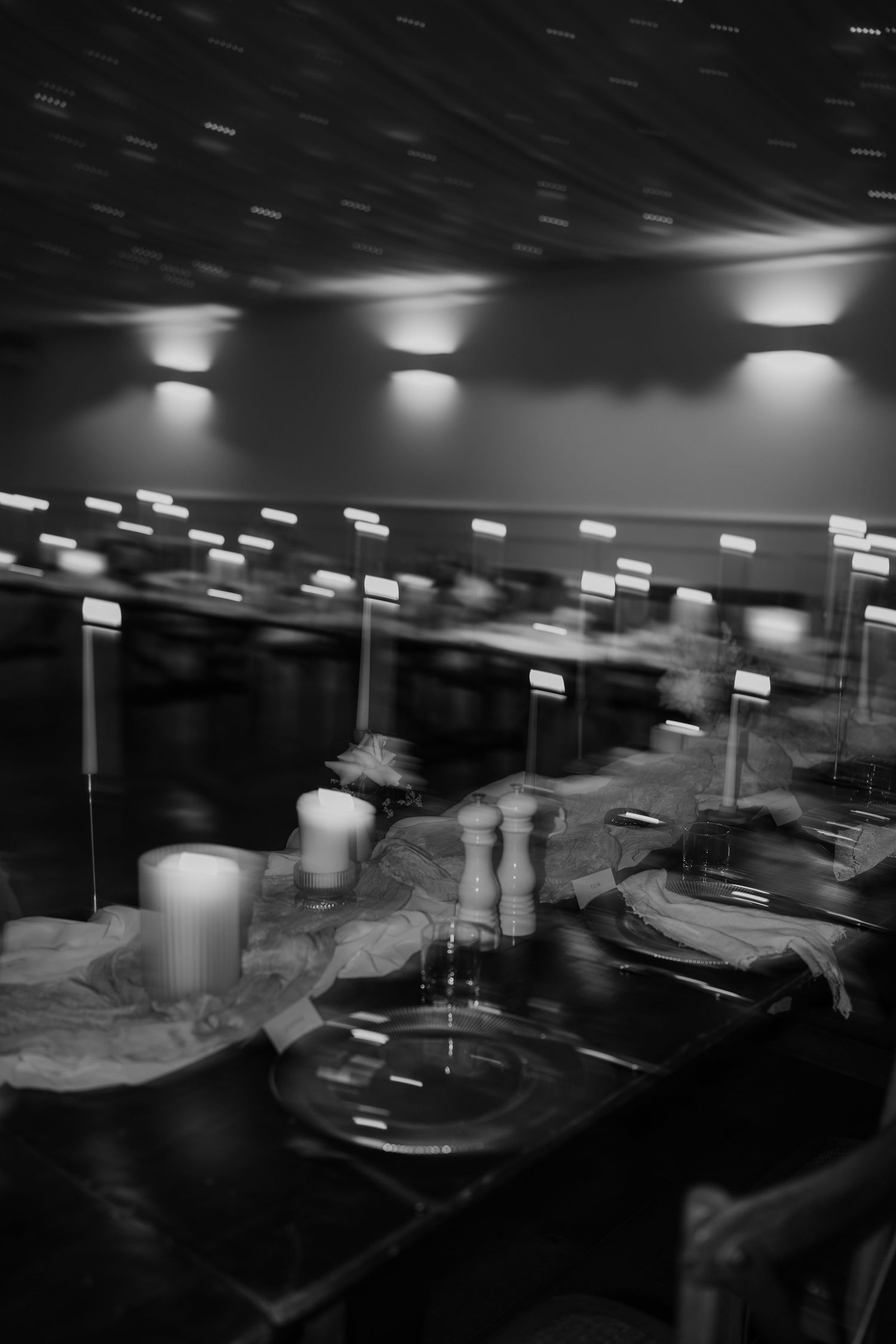 Black and white long exposure photo of a bar setup with blurred motion and overhead spotlights.