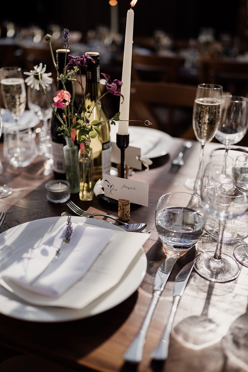 Detail of a wedding table, name tag is in a wine cork with white candles and colourful garden grown flowers.