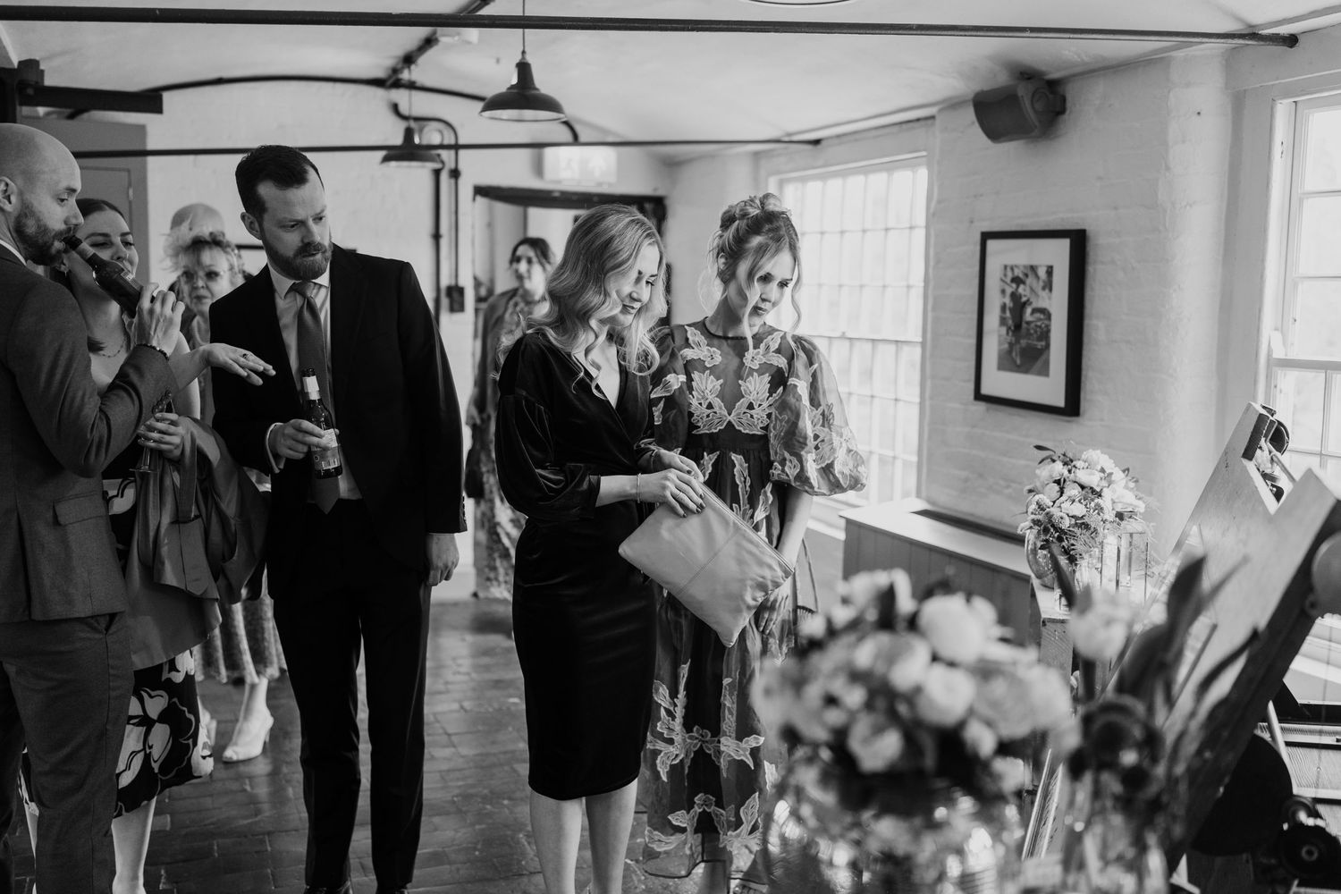 Reception guests mingling near floral arrangements in a bright indoor venue.