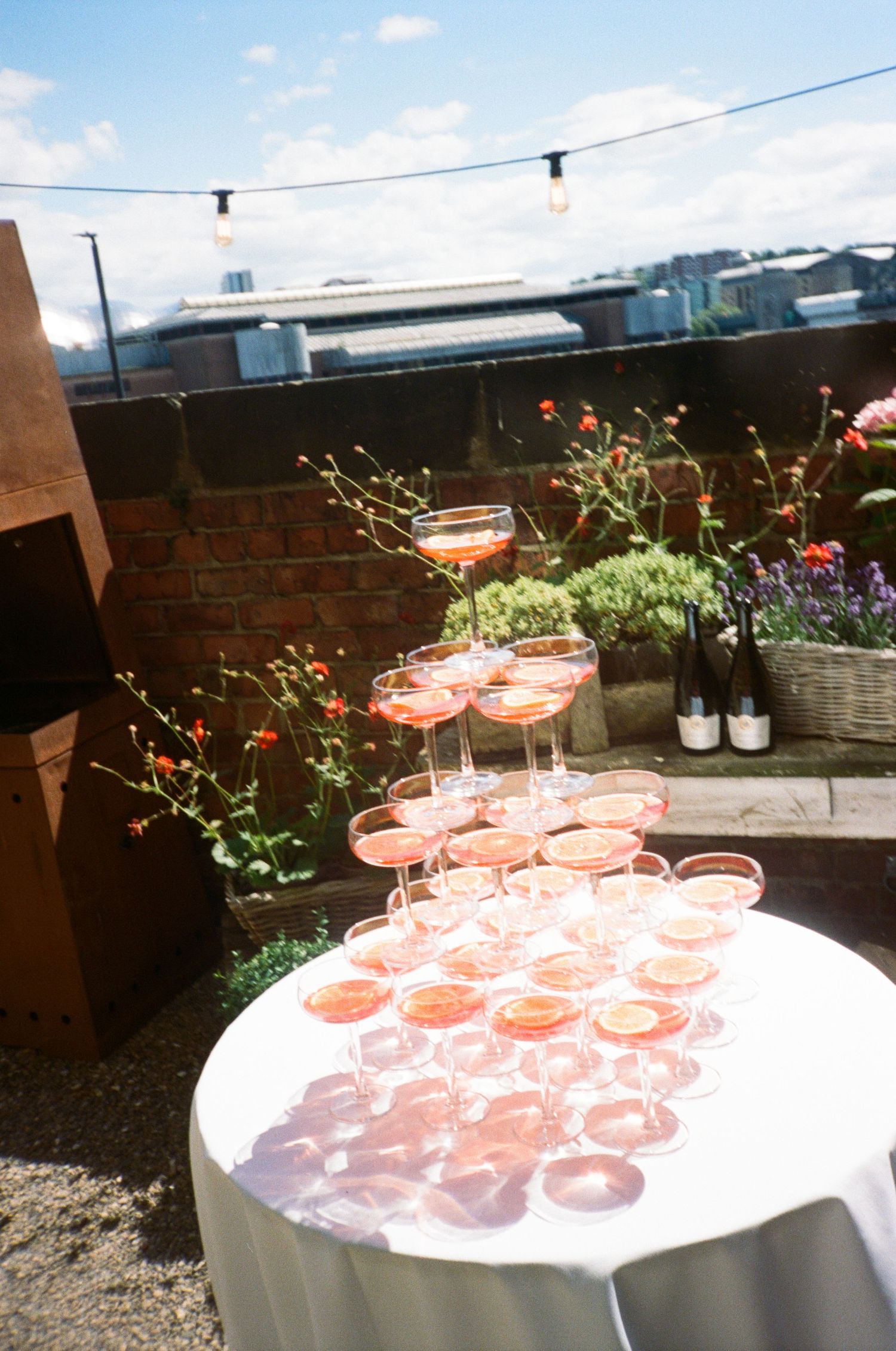 Pink cocktails arranged on a round table at an outdoor rooftop party with string lights and potted flowers.