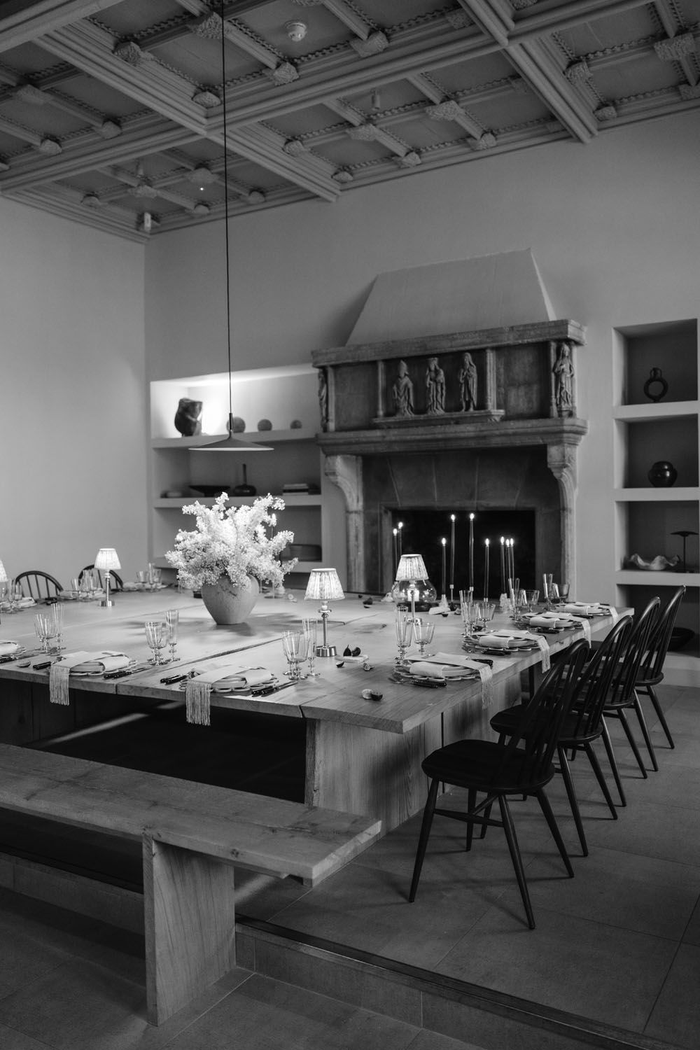 Elegant black and white dining room with long wooden table, candles, floral centerpiece, and ornate stone fireplace.
