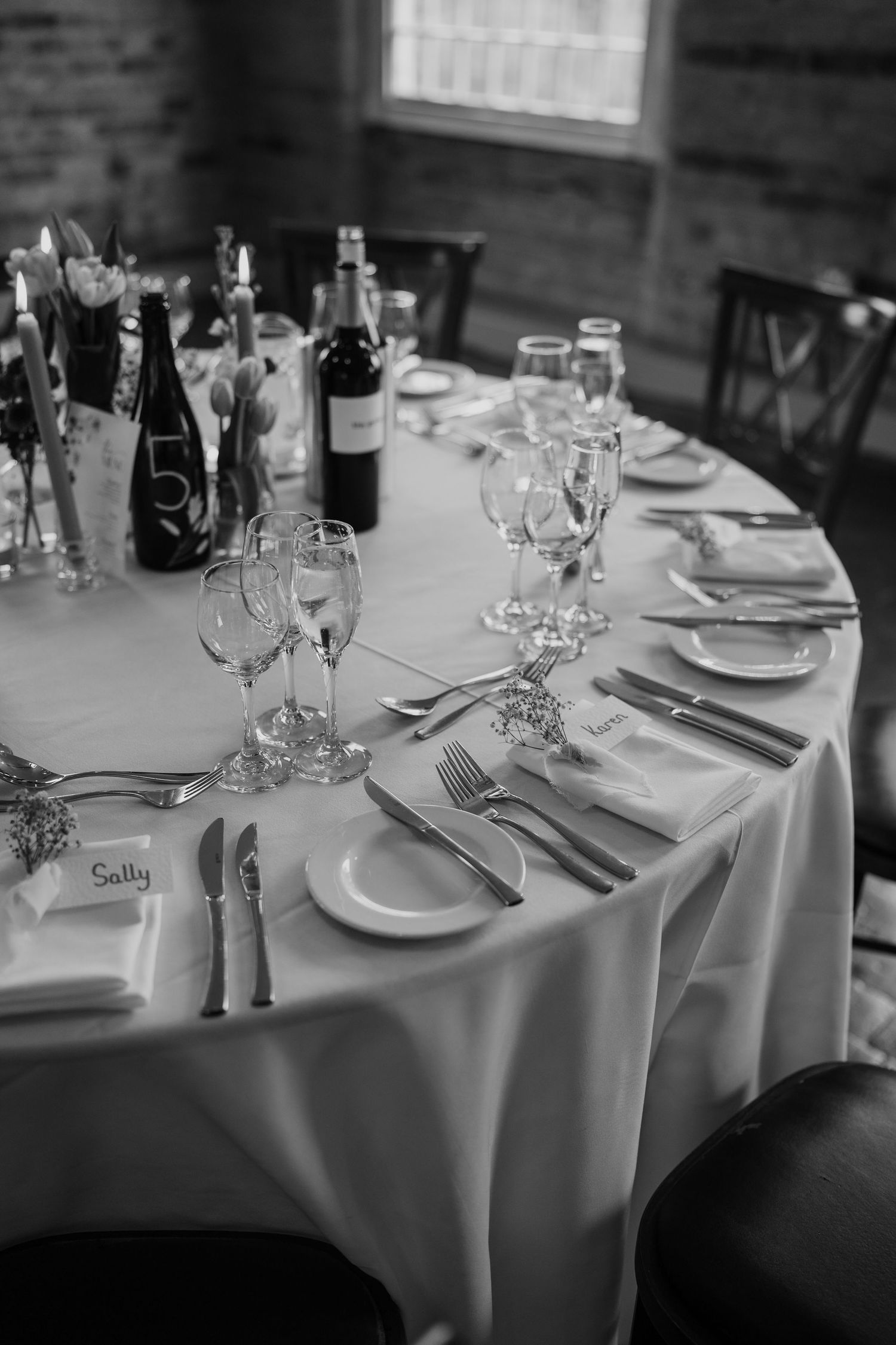 Black and white image of formal place settings at a round table with wine glasses and silverware.