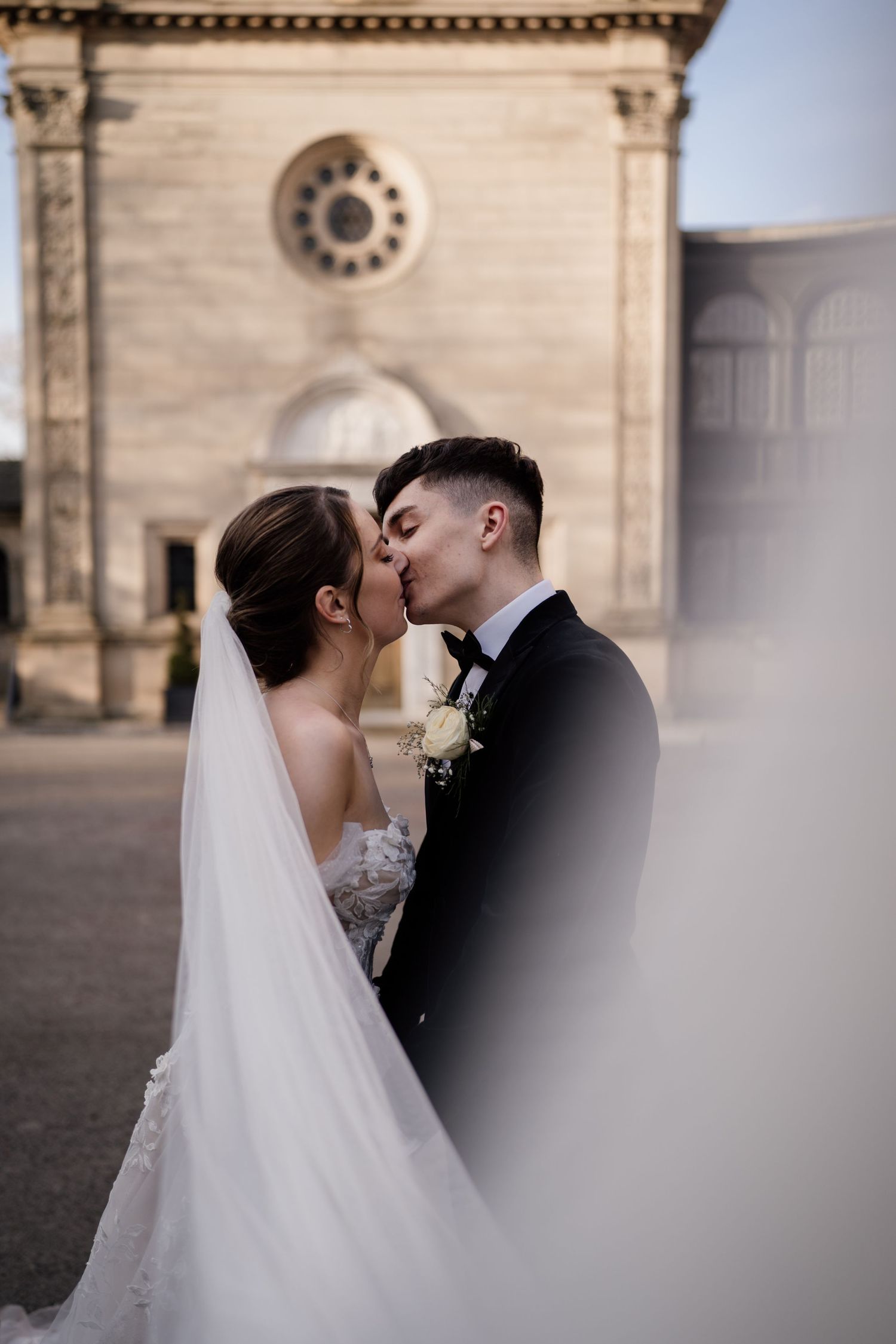 Bride and groom kissing with Bourton Hall in the background and the veil covering some of the photograph.