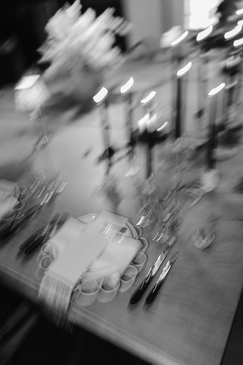 Blurred black and white photo of an elegantly set dining table with plates, cutlery, and glassware at an event.