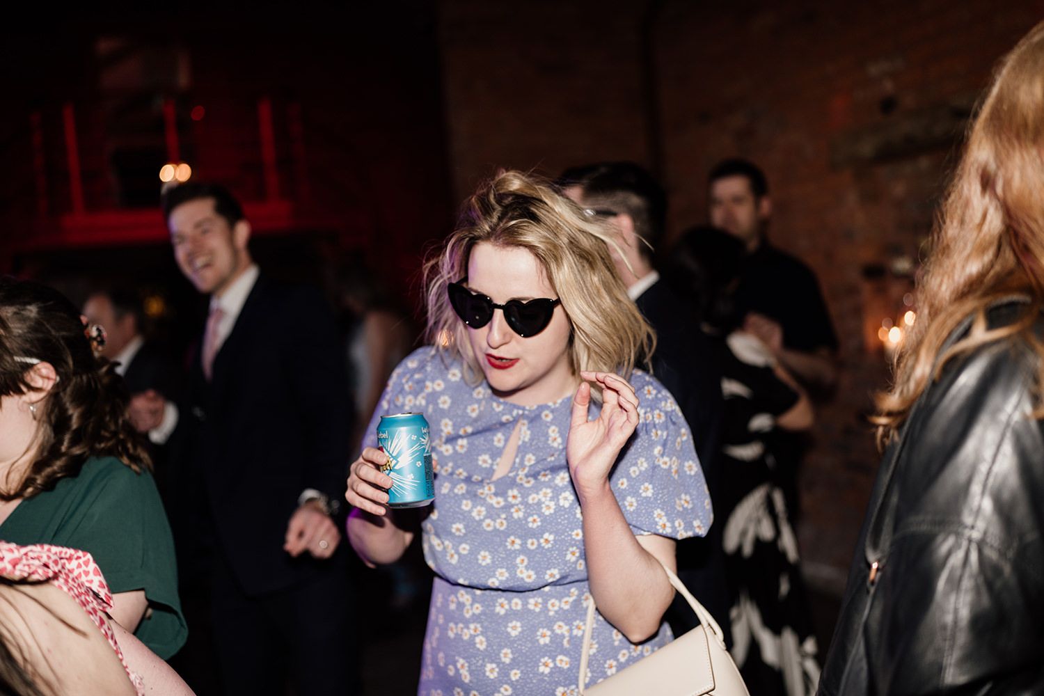 Wedding guest wearing sunglasses and holding a can of beer dancing.