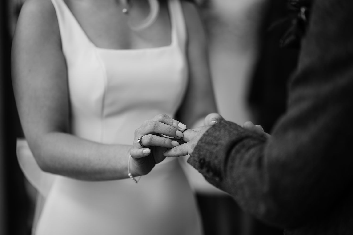 Black and white image of a bride putting a wedding ring on her husbands finger.