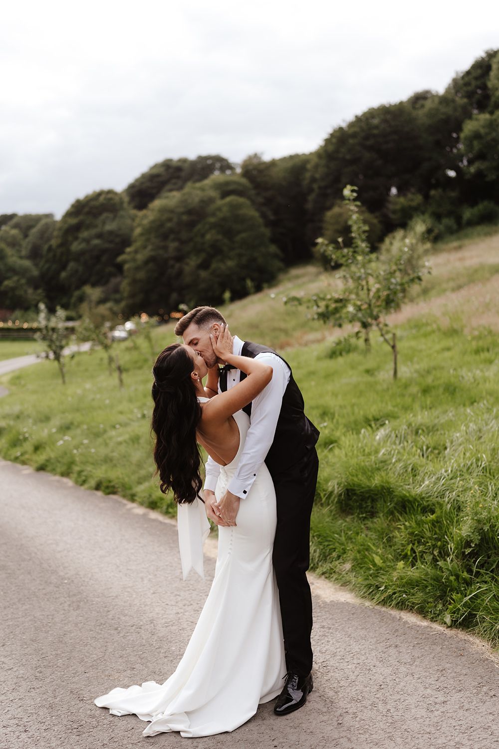 A romantic wedding couple shares intimate moments on a winding path surrounded by lush green hillsides.