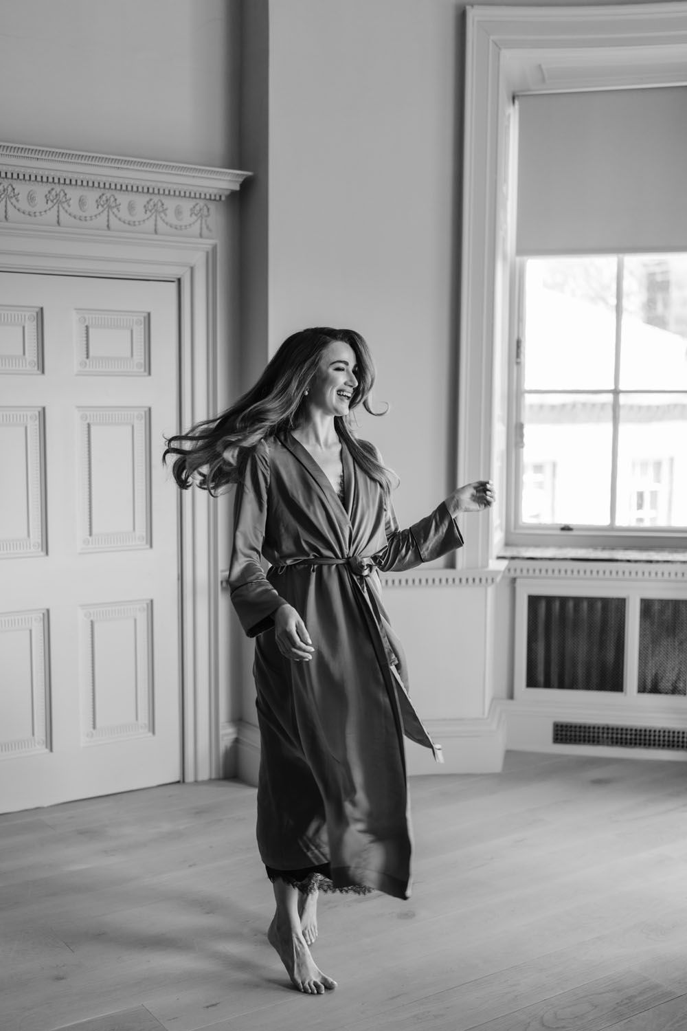 Black and white photo of a smiling woman in a silk robe dancing barefoot in an elegant room.