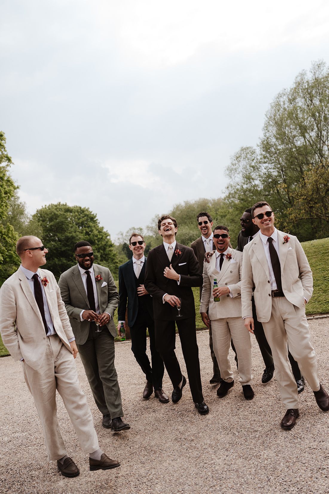 Group of groomsmen in suits and sunglasses walking together outdoors at a wedding celebration.