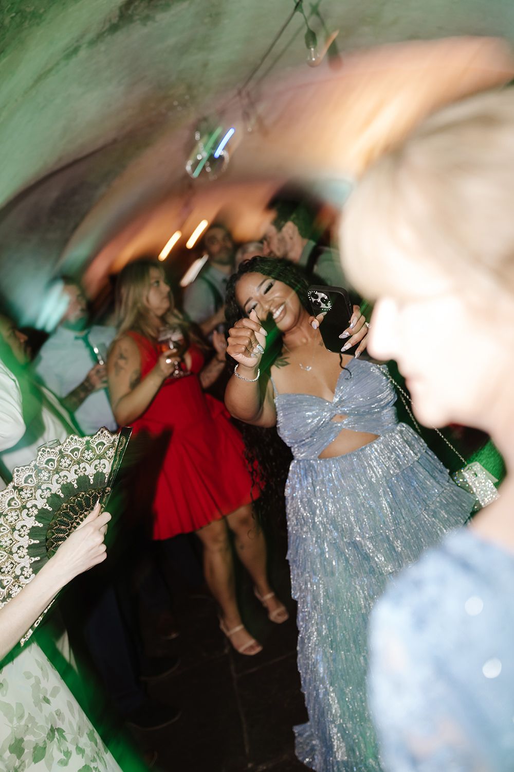 People dancing and celebrating at a lively party with green lighting effects in the background.