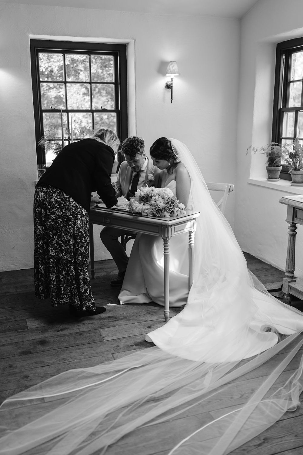 Black and white photo showing a bride signing wedding documents at a table.