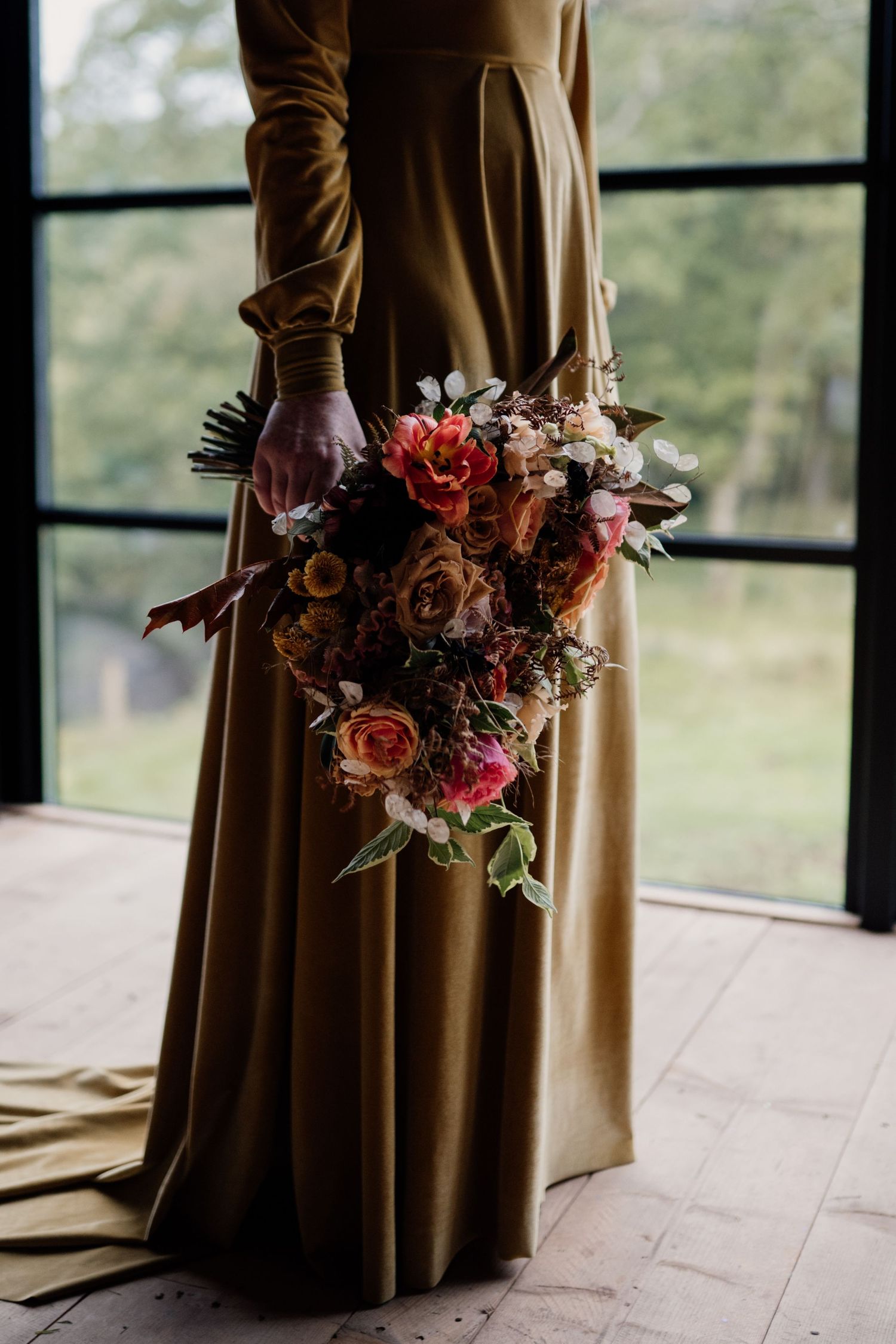 Bride holding her autumnal themed bouquet wearing a mustard wedding dress.