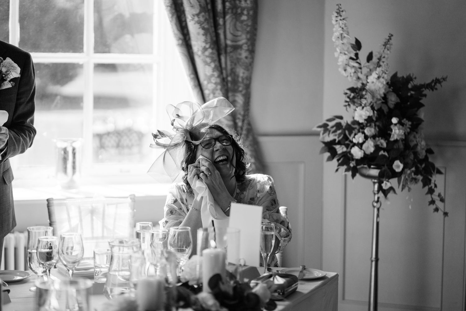 Mother of the bride crying during speeches with flowers behind her.