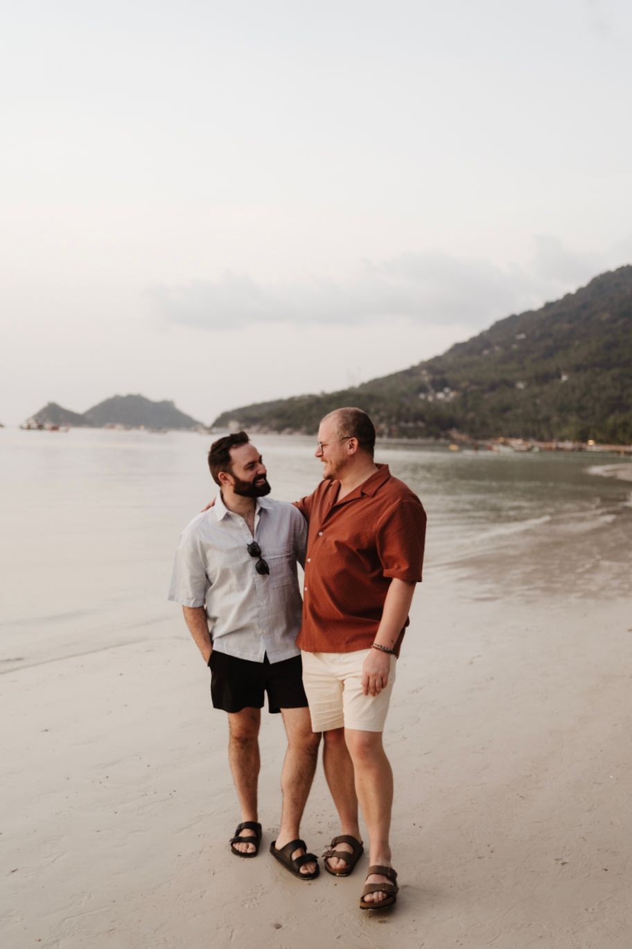 Two men sharing a moment while walking on a tropical beach at dusk.