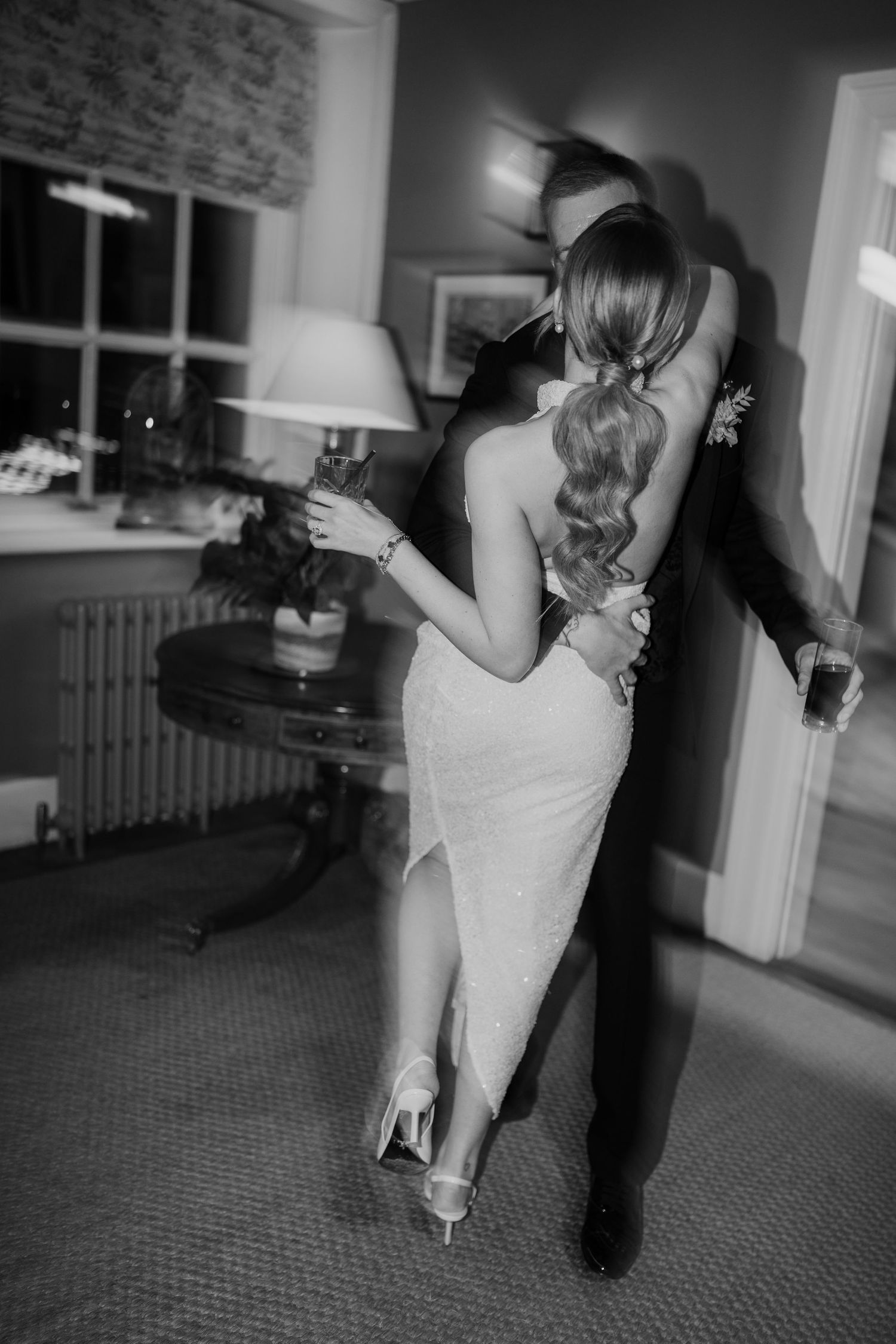 A couple in formal attire dance together in an intimate indoor setting with romantic black and white photography.
