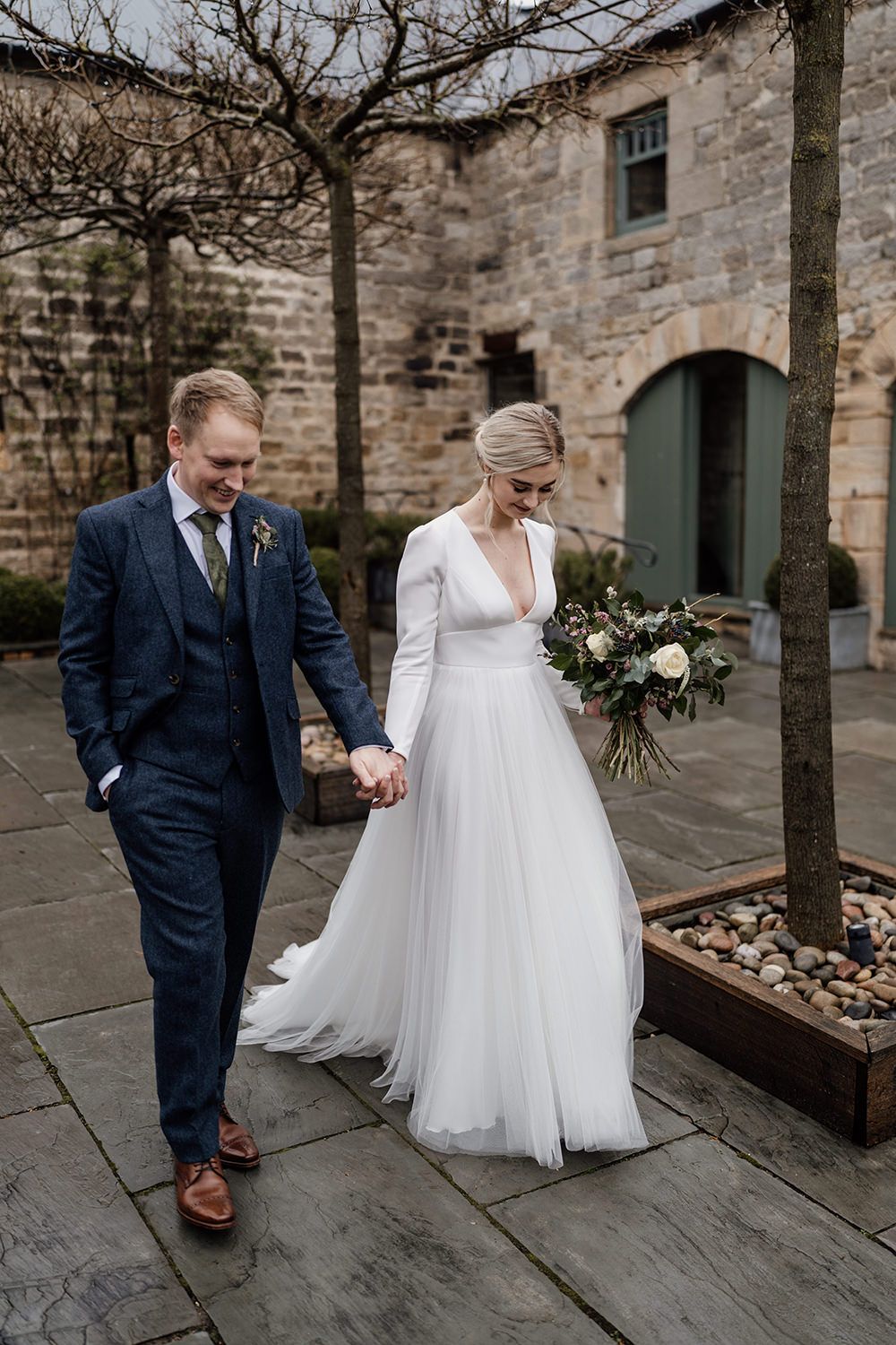 Bride and groom walking towards the camera with Healey Barn in the background.