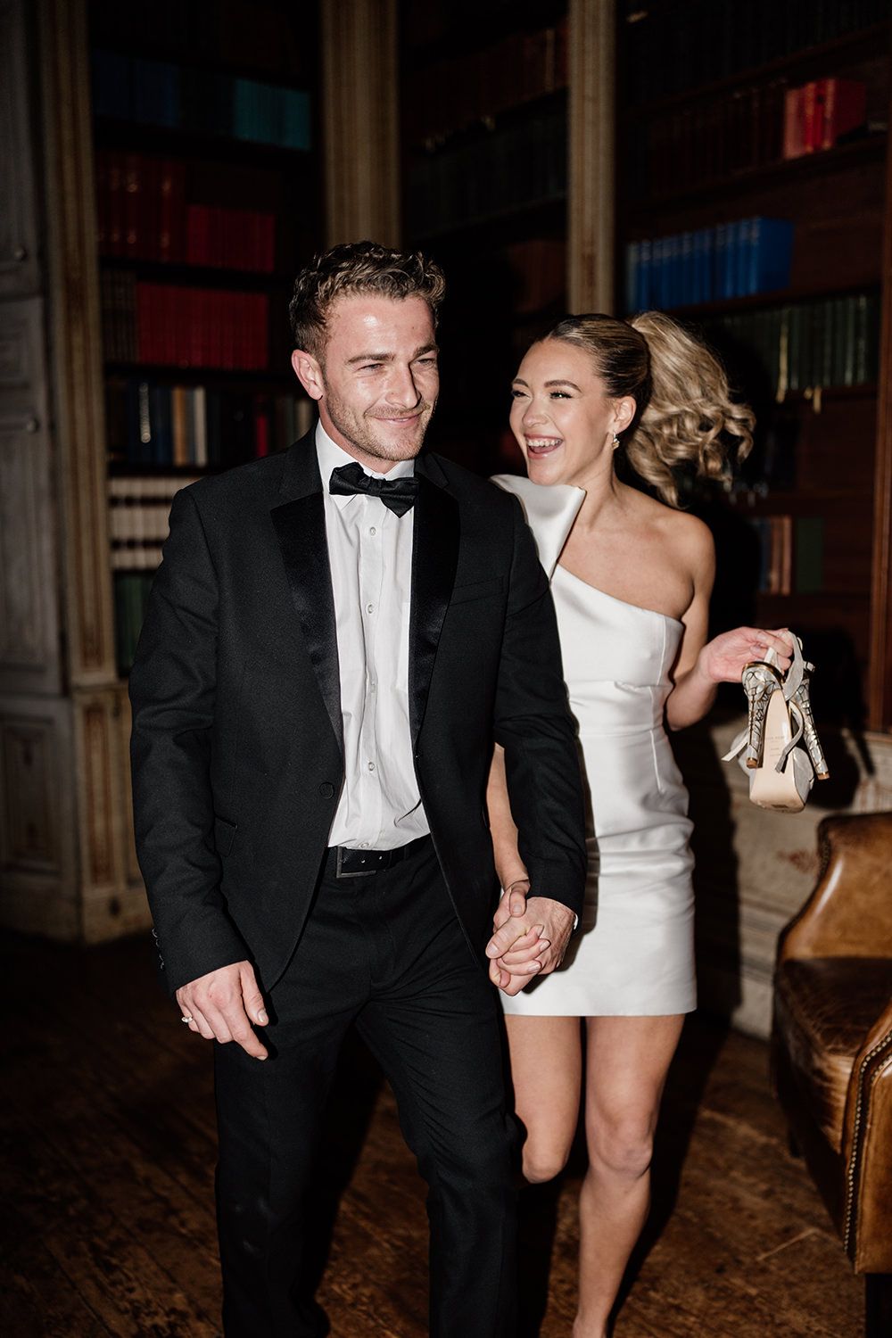 Bride and groom dancing and laughing with each other at night time in the library in Rise Hall.