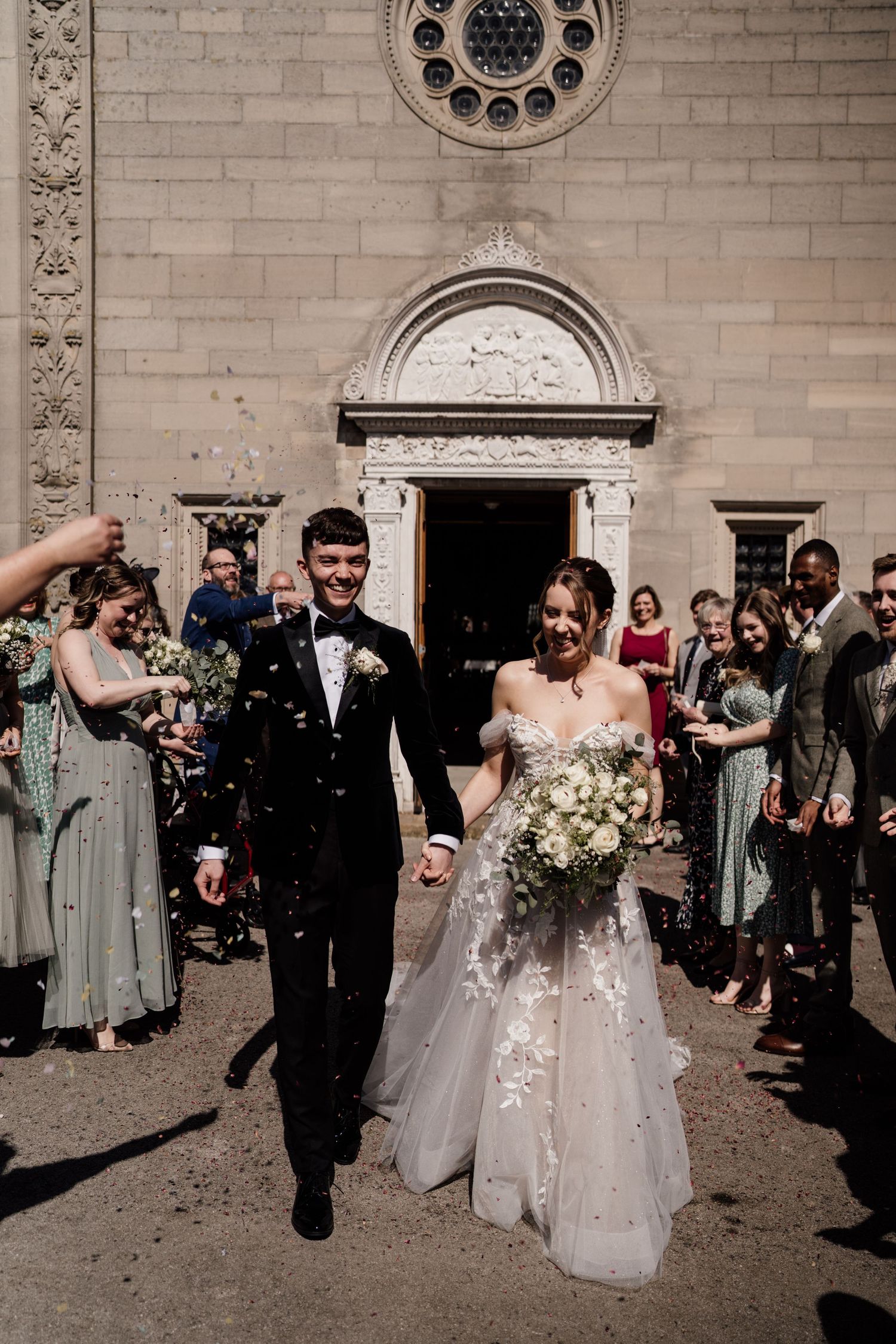 Bride and groom walking through confetti with guests in lines either side.
