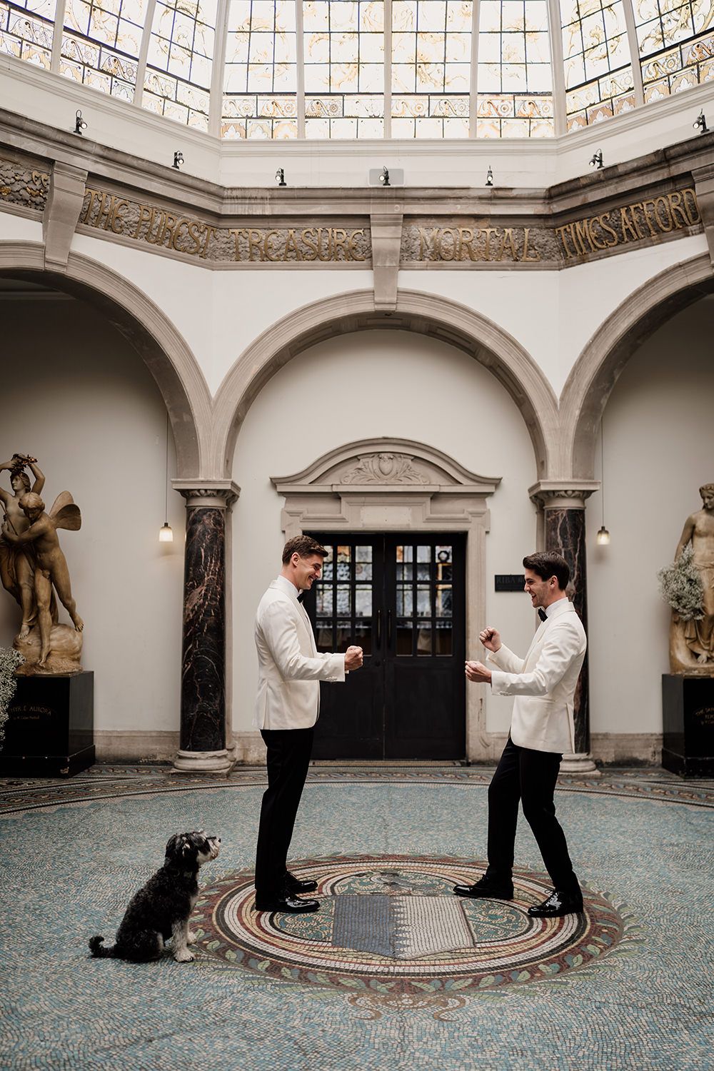 Two grooms cheering after their first look at Battersea Arts Centre. They're wearing white and black tux's.