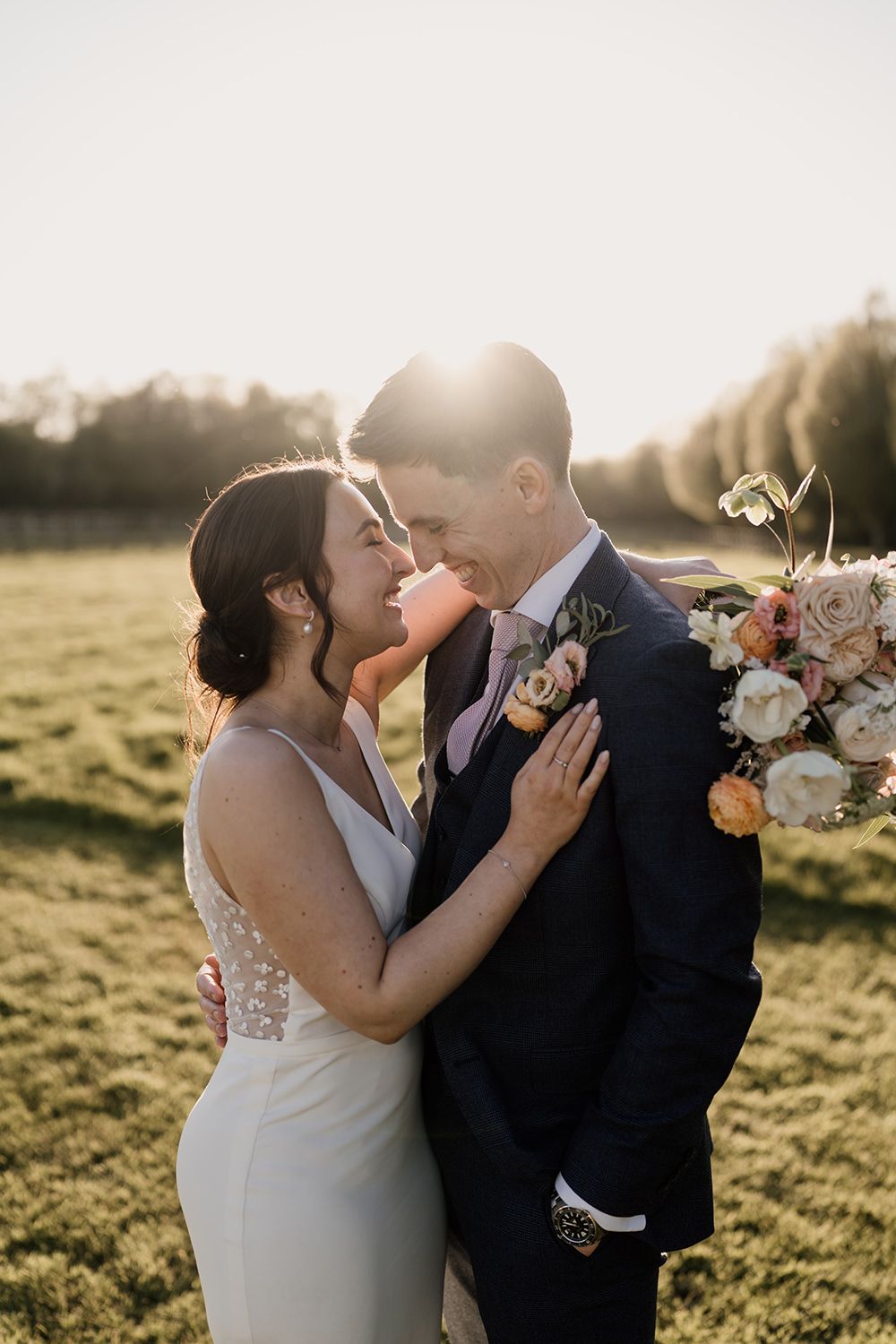 Bride and groom stood looking towards each other with the sun setting, the bride is holding her wedding bouquet.