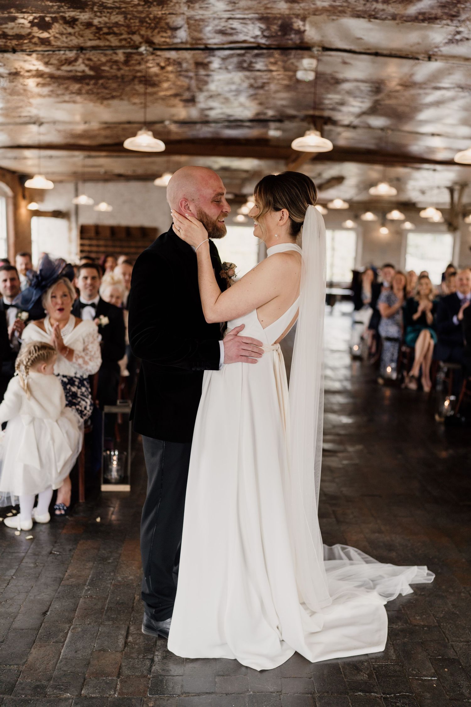 Romantic first dance moment in rustic venue with pendant lights and wooden beams.