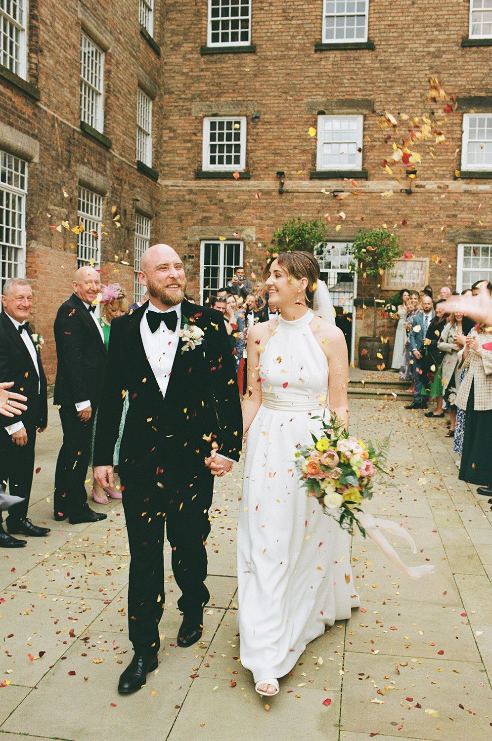 Bride and groom walking through confetti with wedding guests cheering.