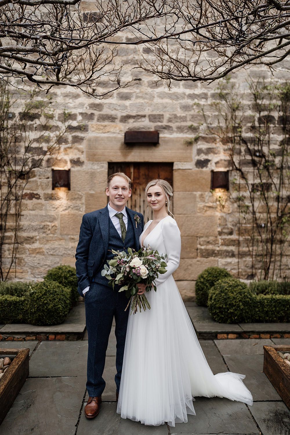 Bride and groom stood looking towards the camera with Healey Barn in the background.