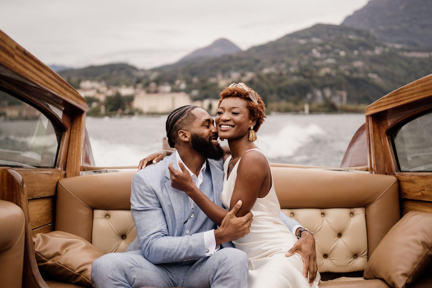 Bride and groom laughing together on a luxury wooden boat on Lake Como, Italy.