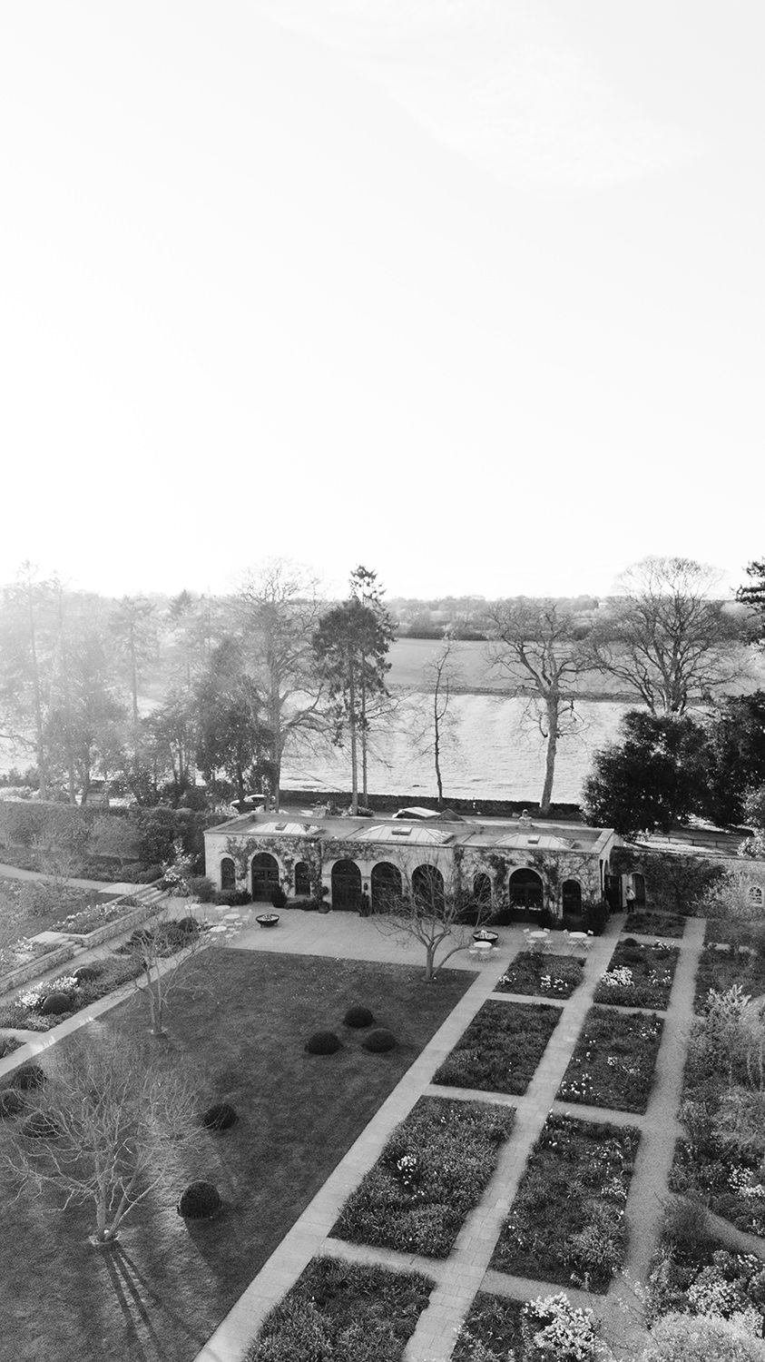 Aerial black and white vintage photograph of a garden with arched colonnade and geometric landscaping overlooking a lake.