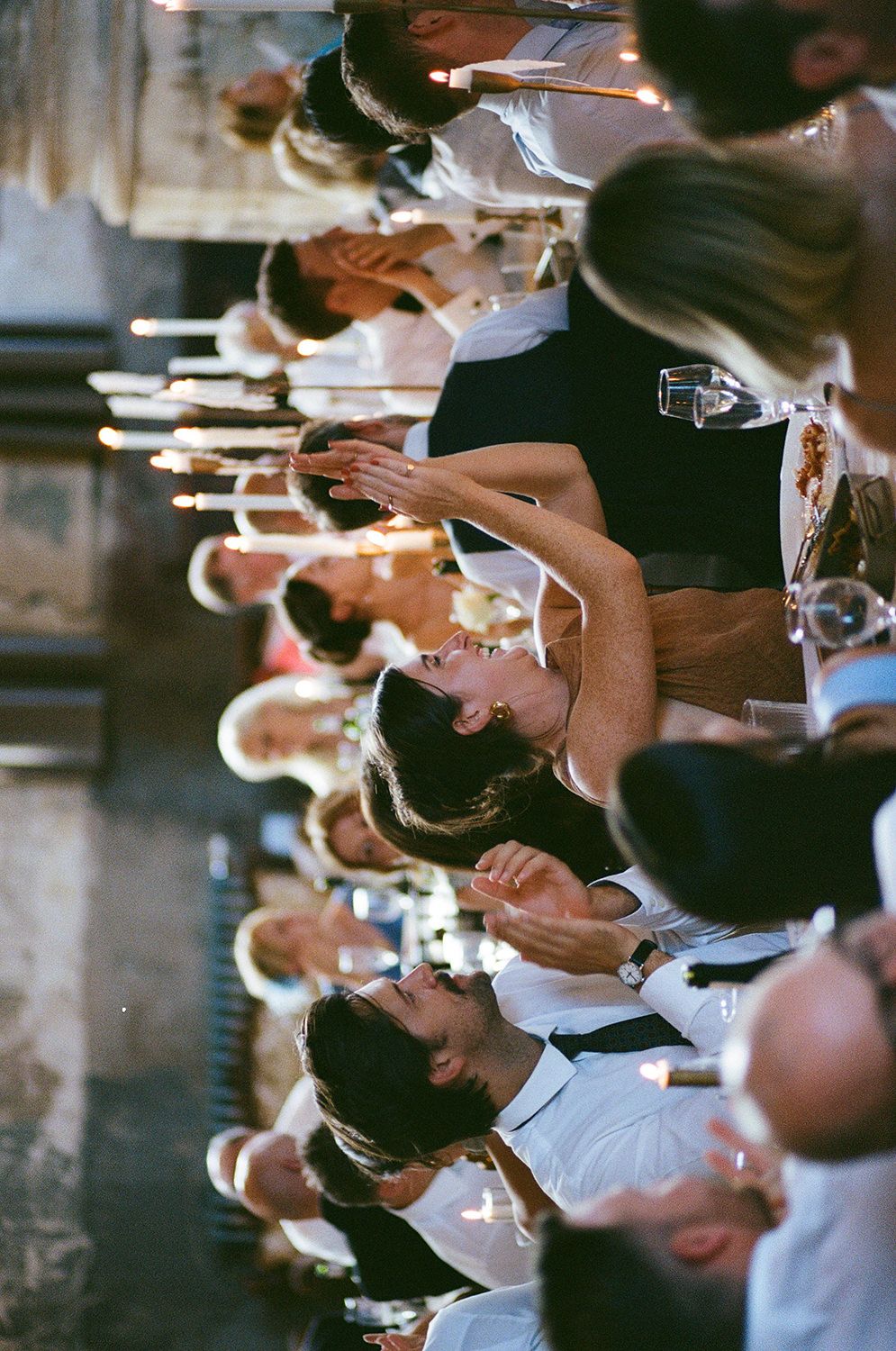 Servers in formal black and white attire carrying wine glasses and plates in a dimly lit restaurant setting.