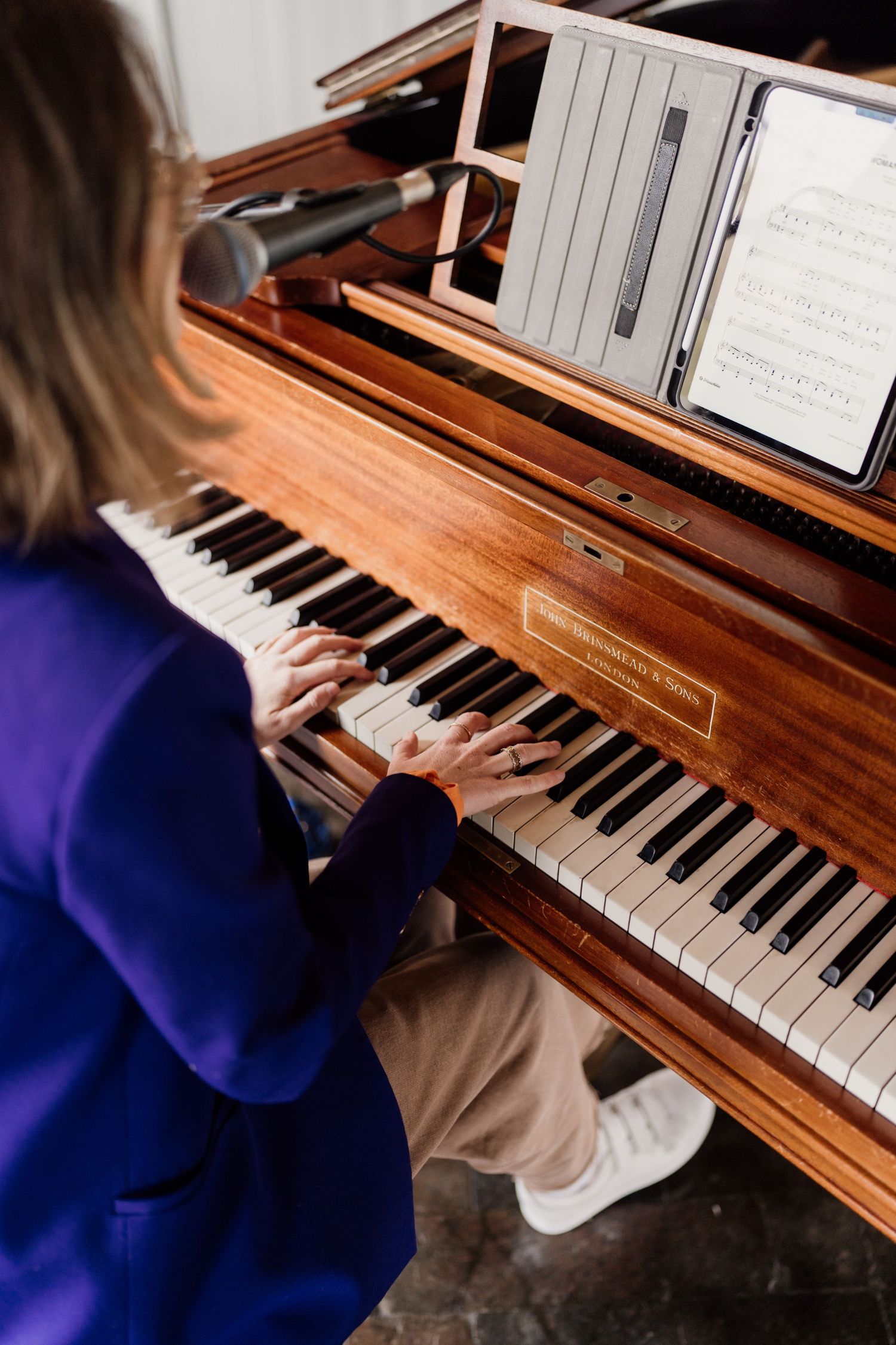 Person in blue sweater playing a wooden piano with sheet music displayed.
