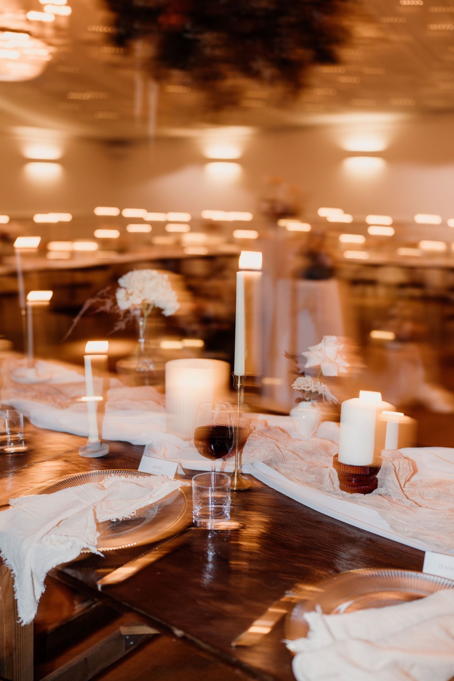 Rustic wedding table setting with white candles, lace runners and warm ambient lighting.