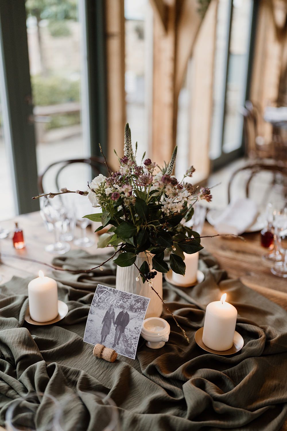 Wedding reception table styled with green fabric, candles, photographs and wine glasses.