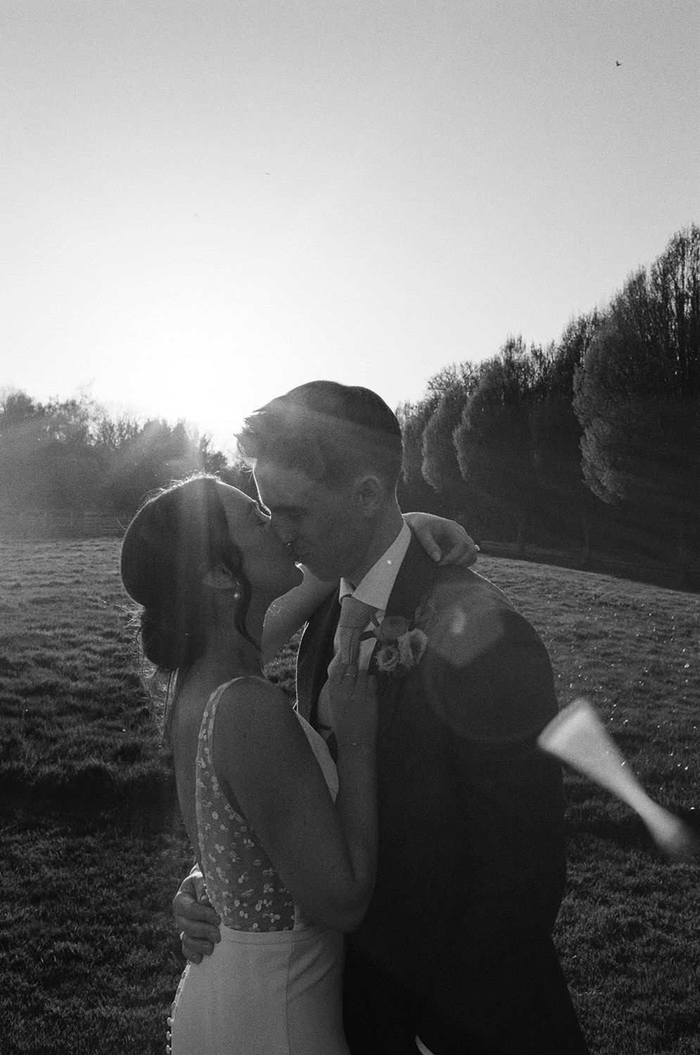 Black and white 35mm film image of couple kissing with the sun setting behind them in black and white.