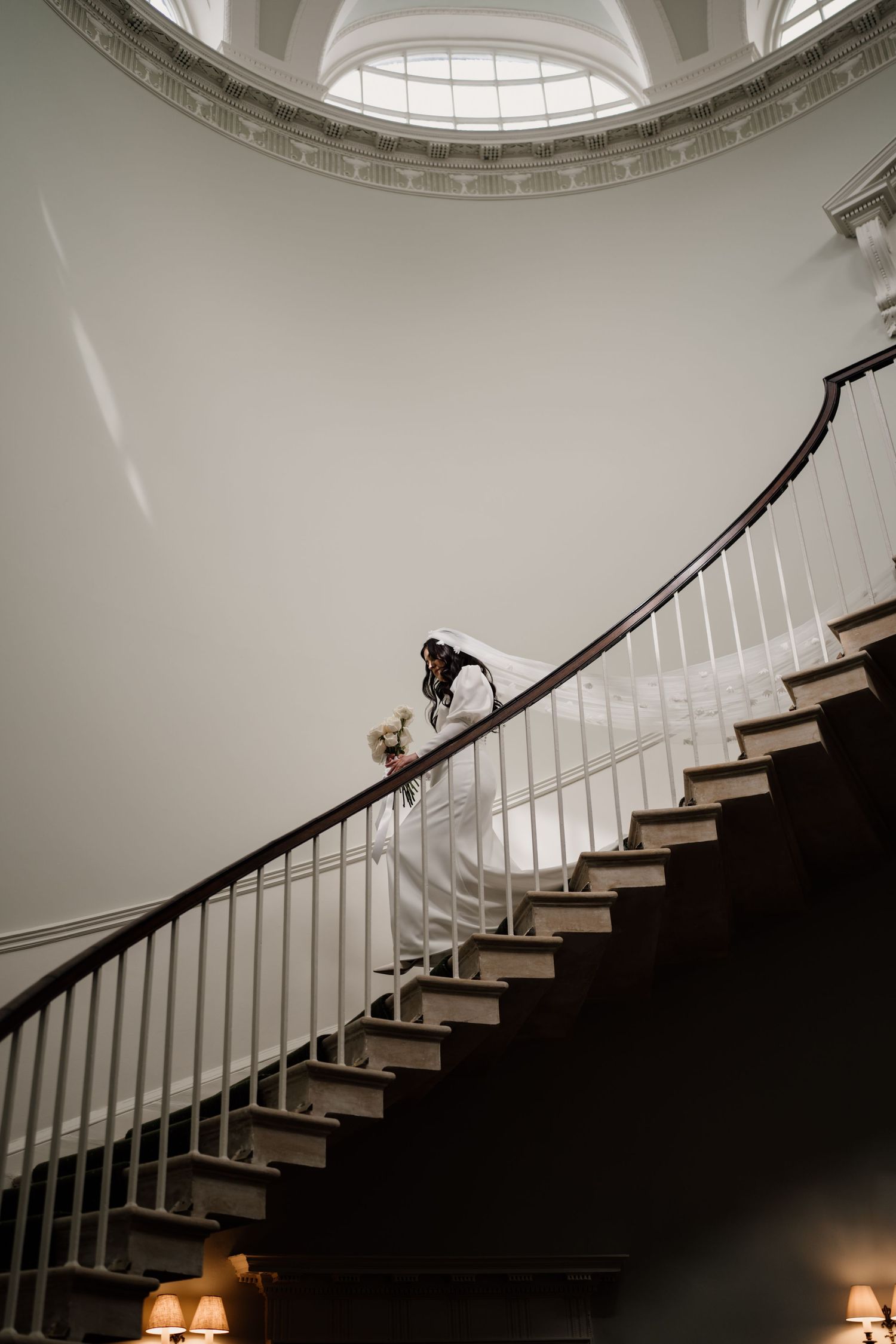 Bride walking down a curved staircase to her wedding ceremony at Middleton Lodge Estate.