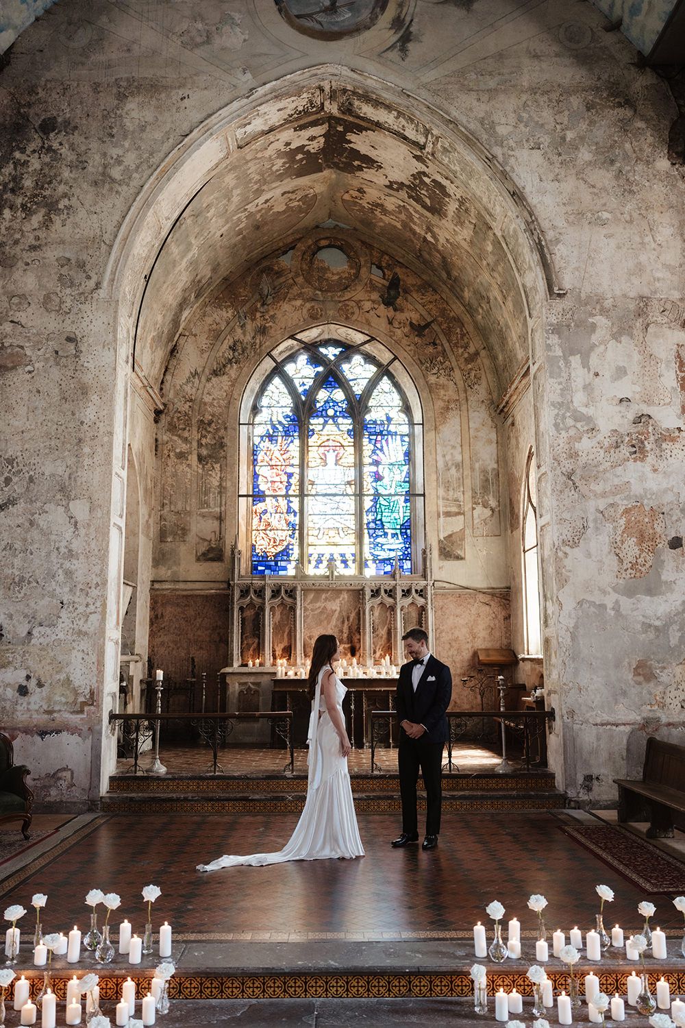 Wedding ceremony in an atmospheric old stone church with stained glass windows and candle-lined aisle.