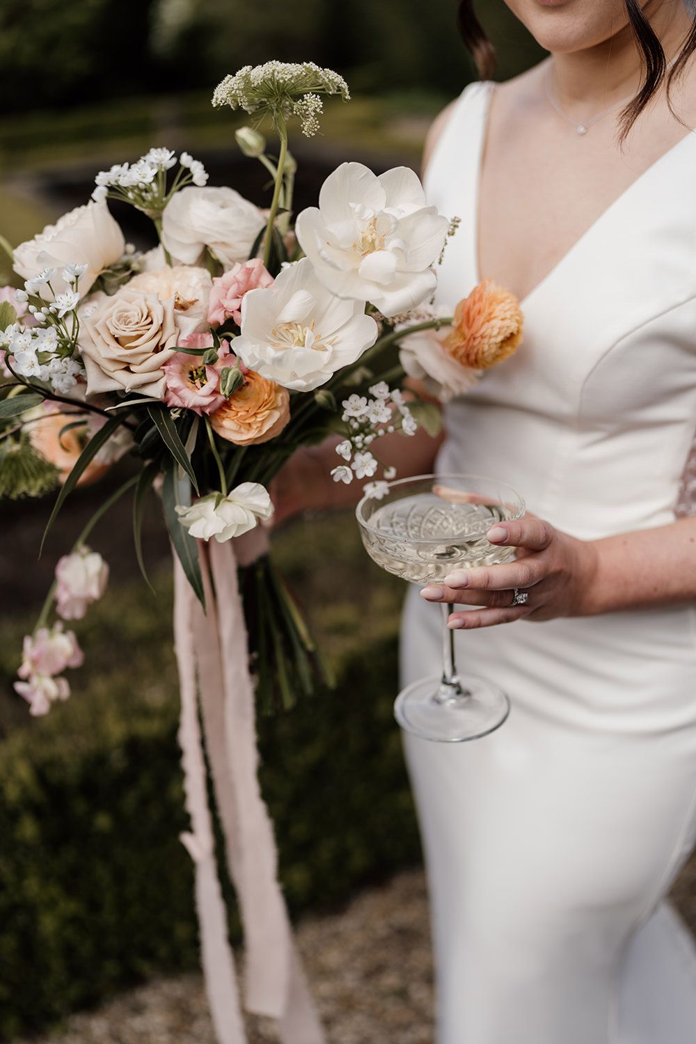 Bride stood holding her wedding flowers and a glass of champagne on her wedding day.