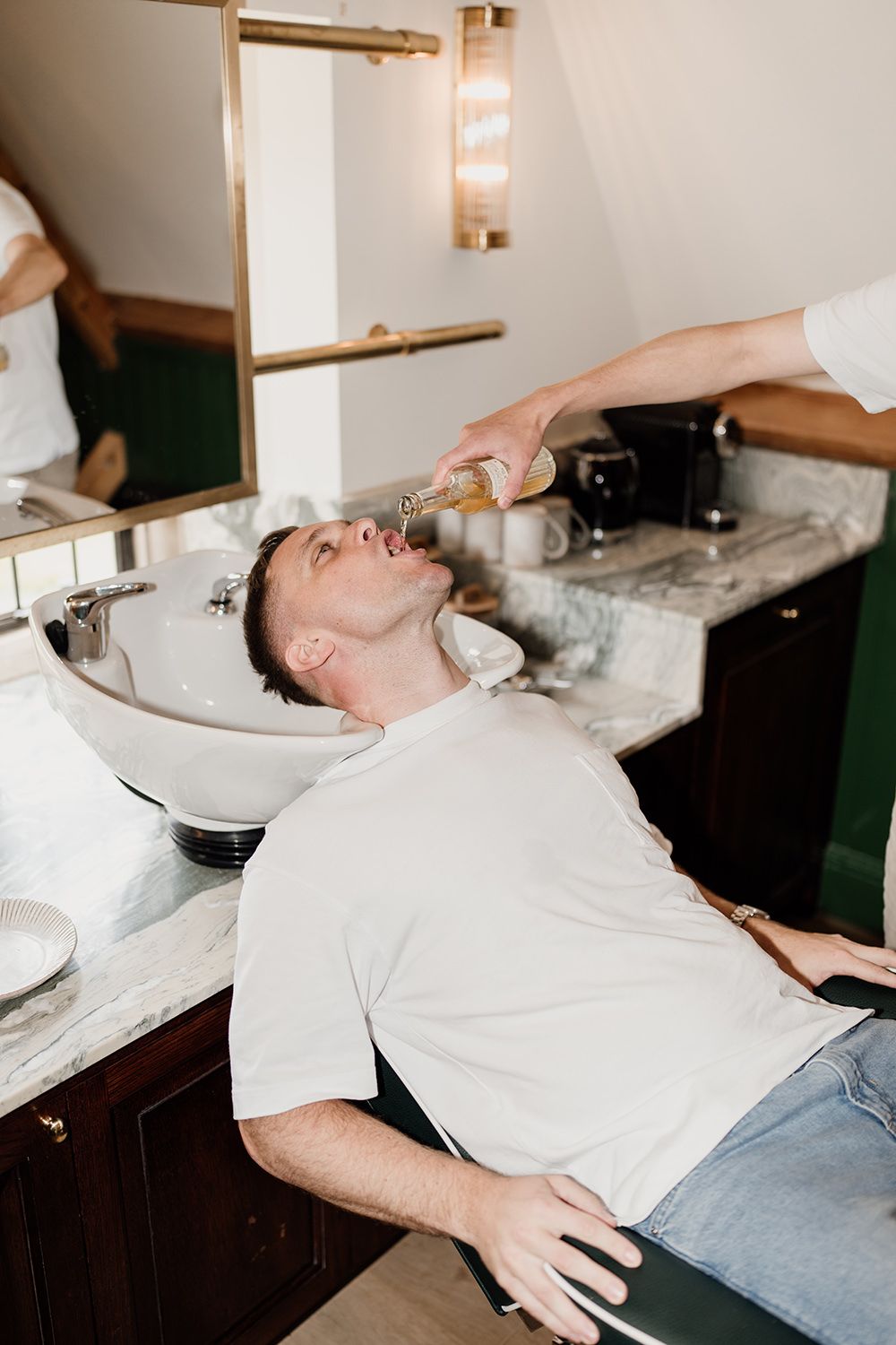Groom in the barbers at kin house as groomsmen pour him beer.