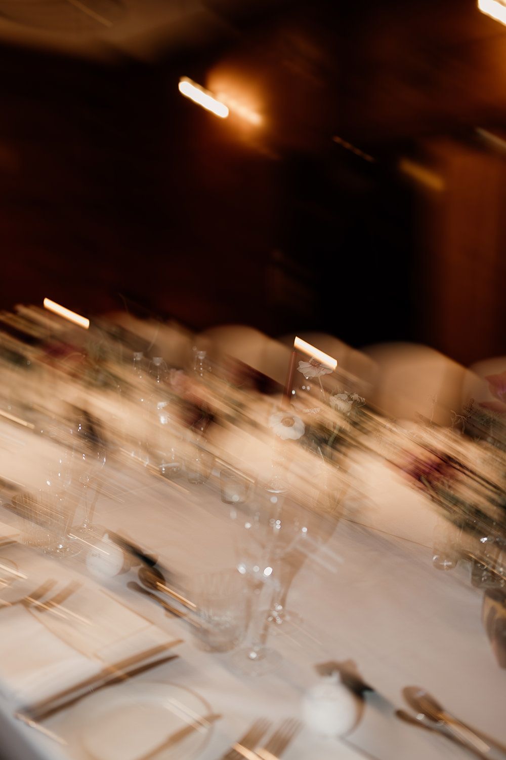 Motion-blurred image of an elegant table setting with wine glasses and place settings in warm lighting.