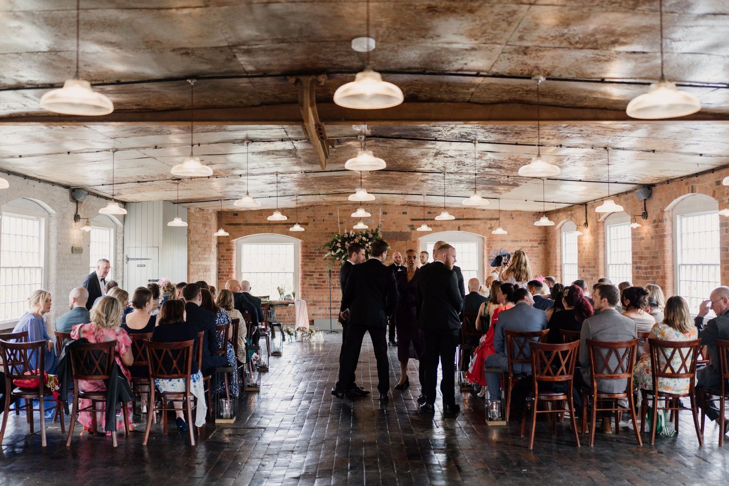 Wedding ceremony in a rustic industrial venue with exposed brick walls and pendant lighting.