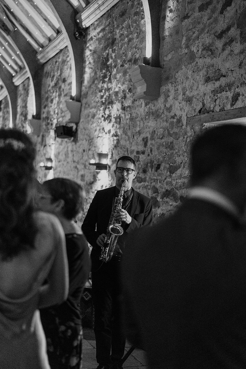 Man playing his saxophone for guests at wedding reception in black and white.