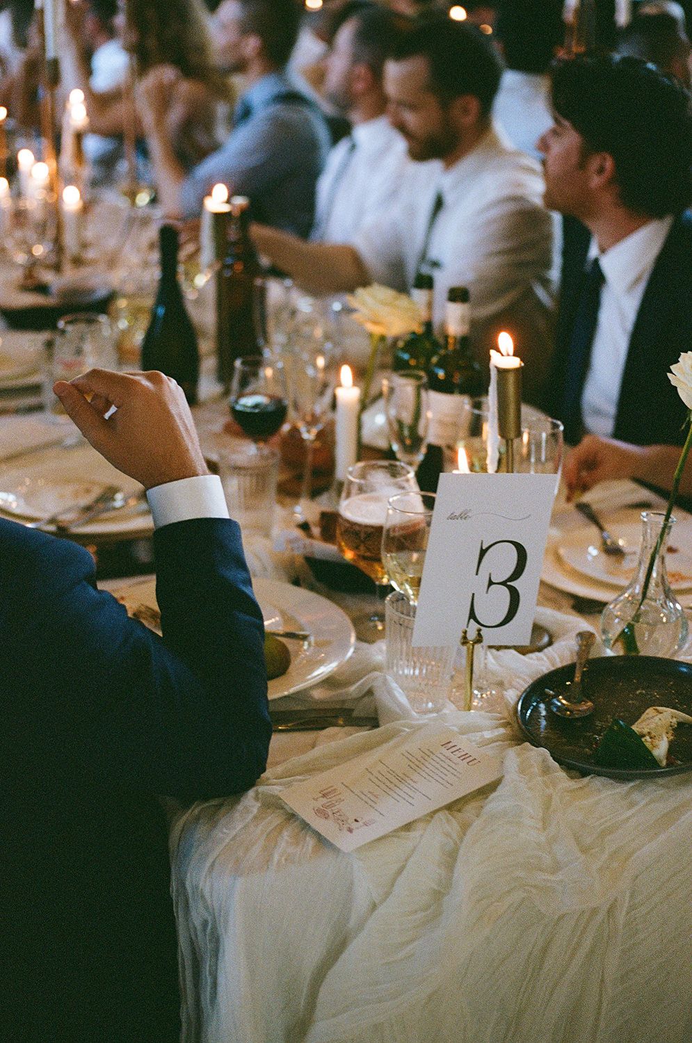 Wedding reception tables decorated with candlelight and table numbers create an elegant dining atmosphere.