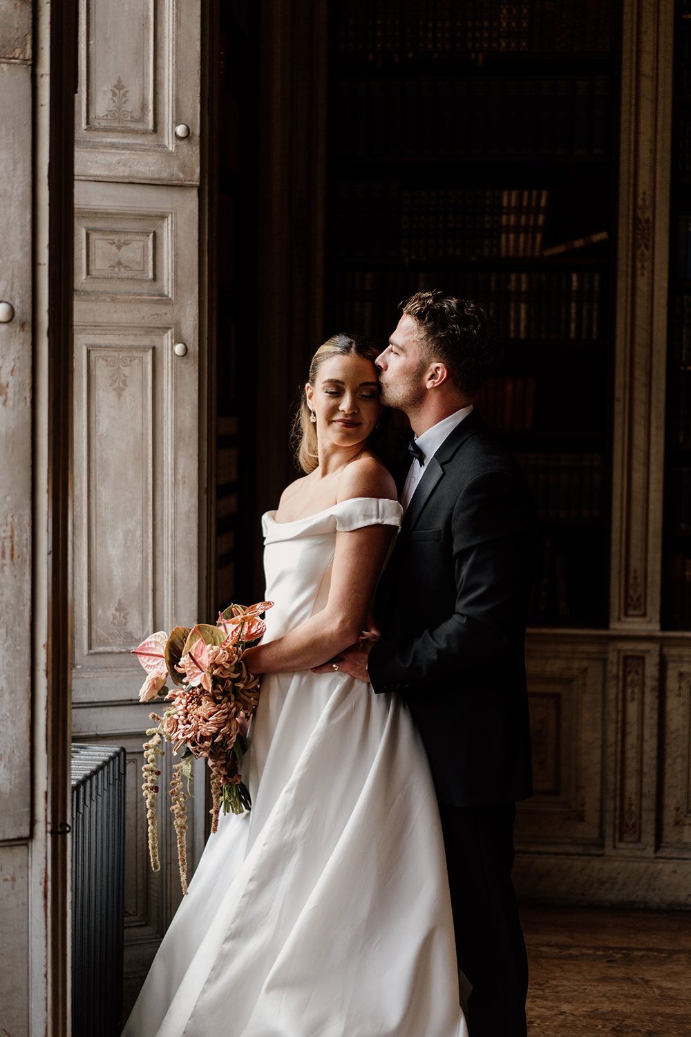 Bride and groom face towards each other while being lit by a grand window at Rise Hall.