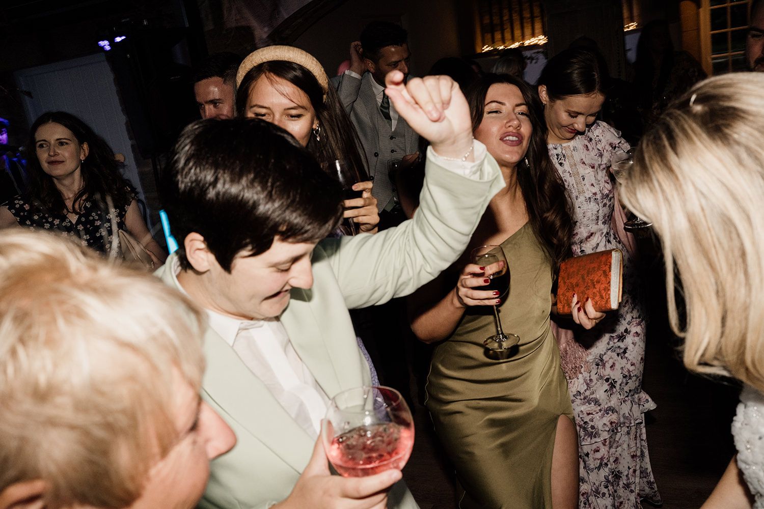 Bridesmaid dancing in a mint green suit, other guests are around celebrating.