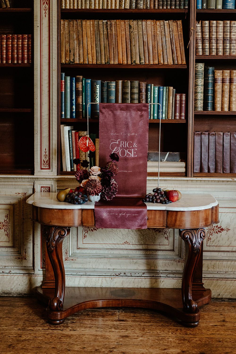 Wedding flowers and stationery on a wooden table in the library at Rise Hall.