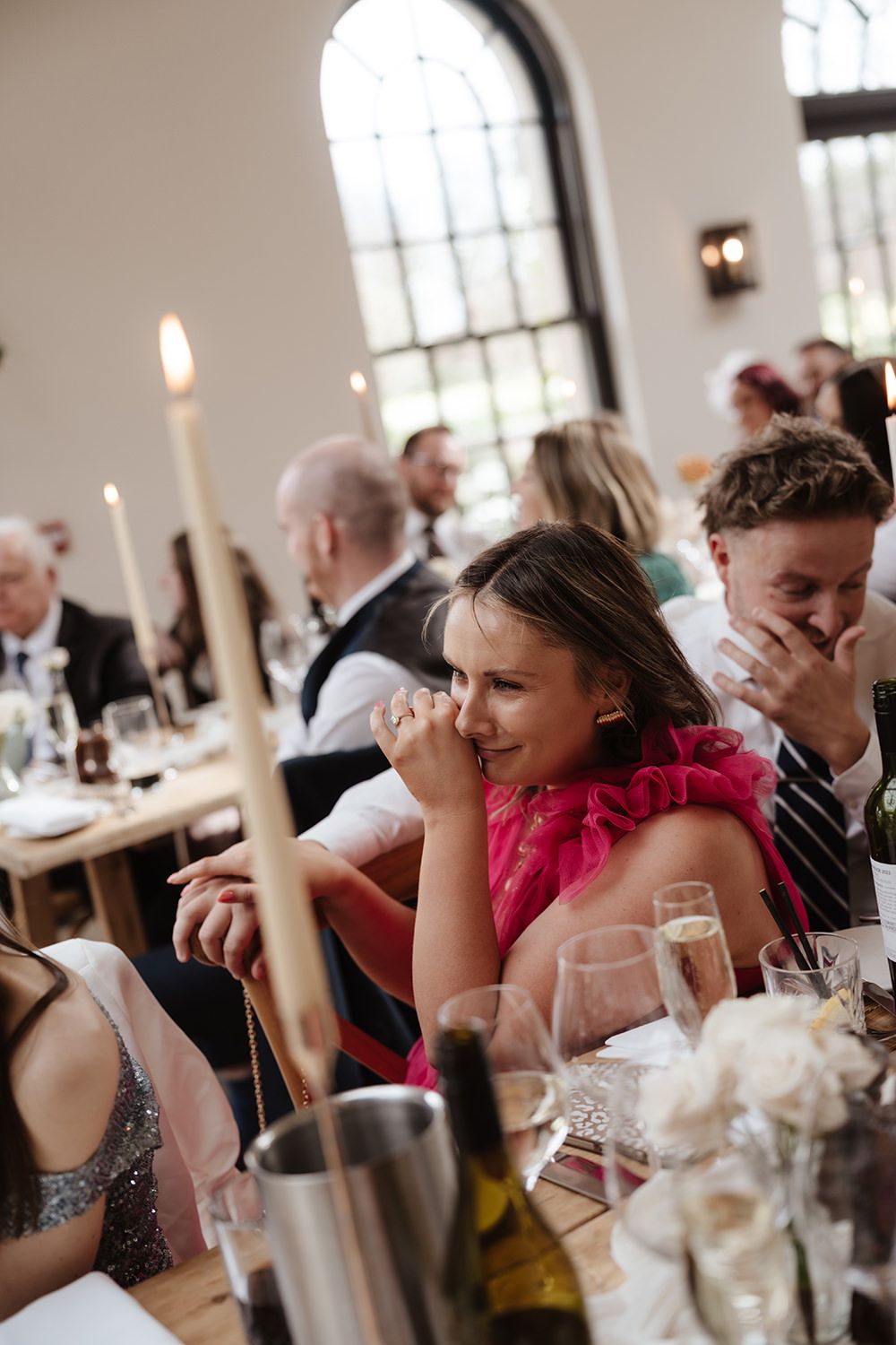 A candid moment during a wedding reception in a venue with arched windows and candles on the dining tables.