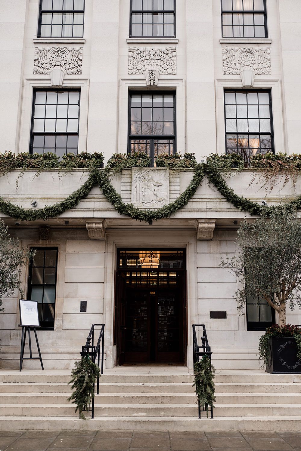 White stone building entrance decorated with cascading evergreen garland swags and winter holiday greenery.