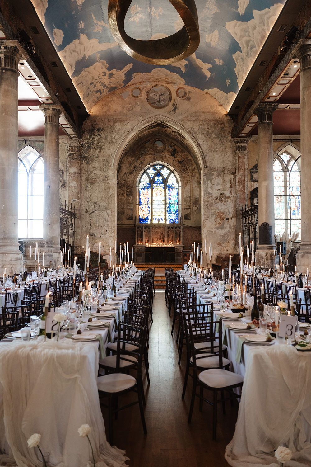 Panoramic view of an elegant wedding reception setup in a historic chapel with vaulted ceilings and stained glass windows.