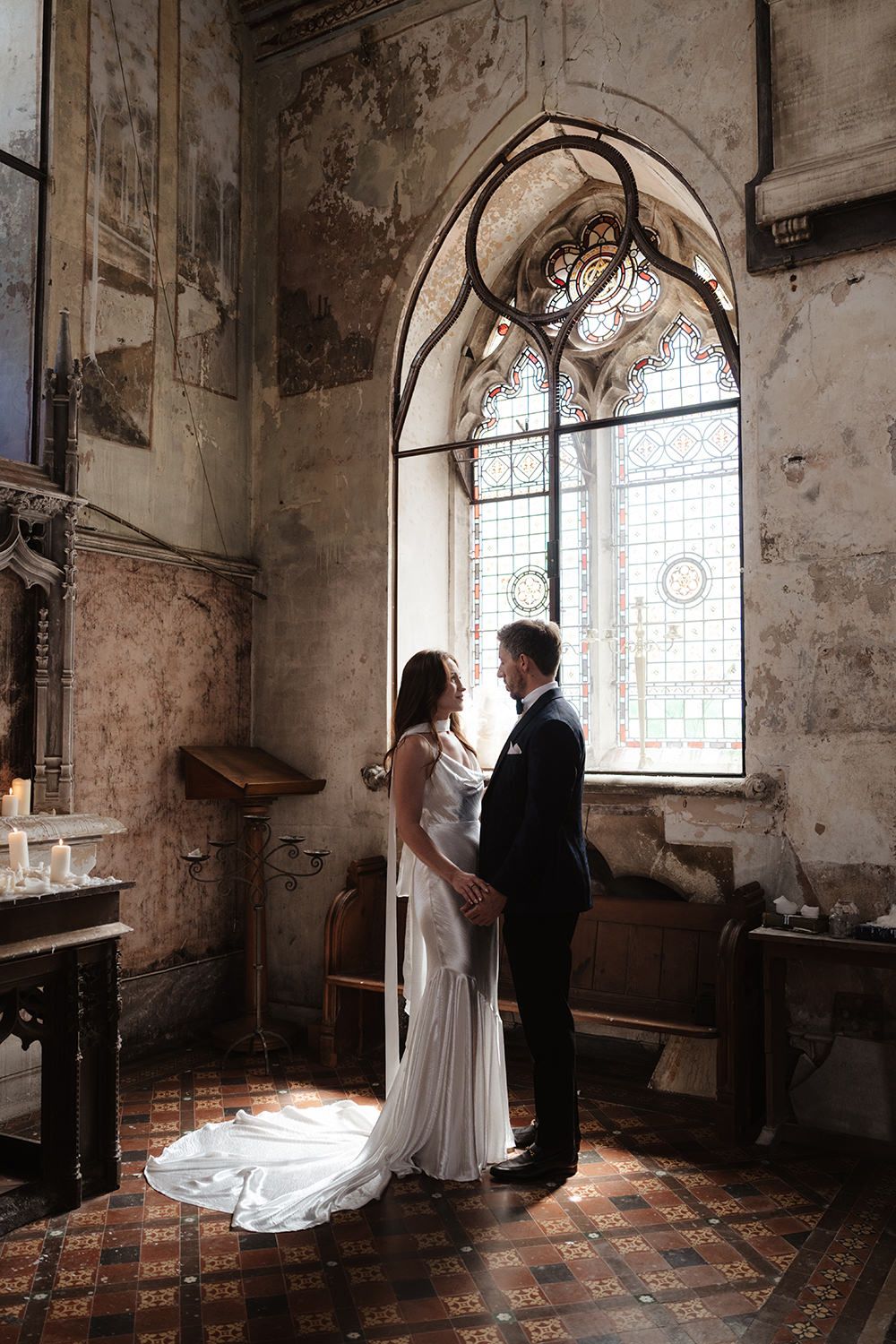 Dramatic wedding photography in a historic church interior with arched windows and weathered stone walls.