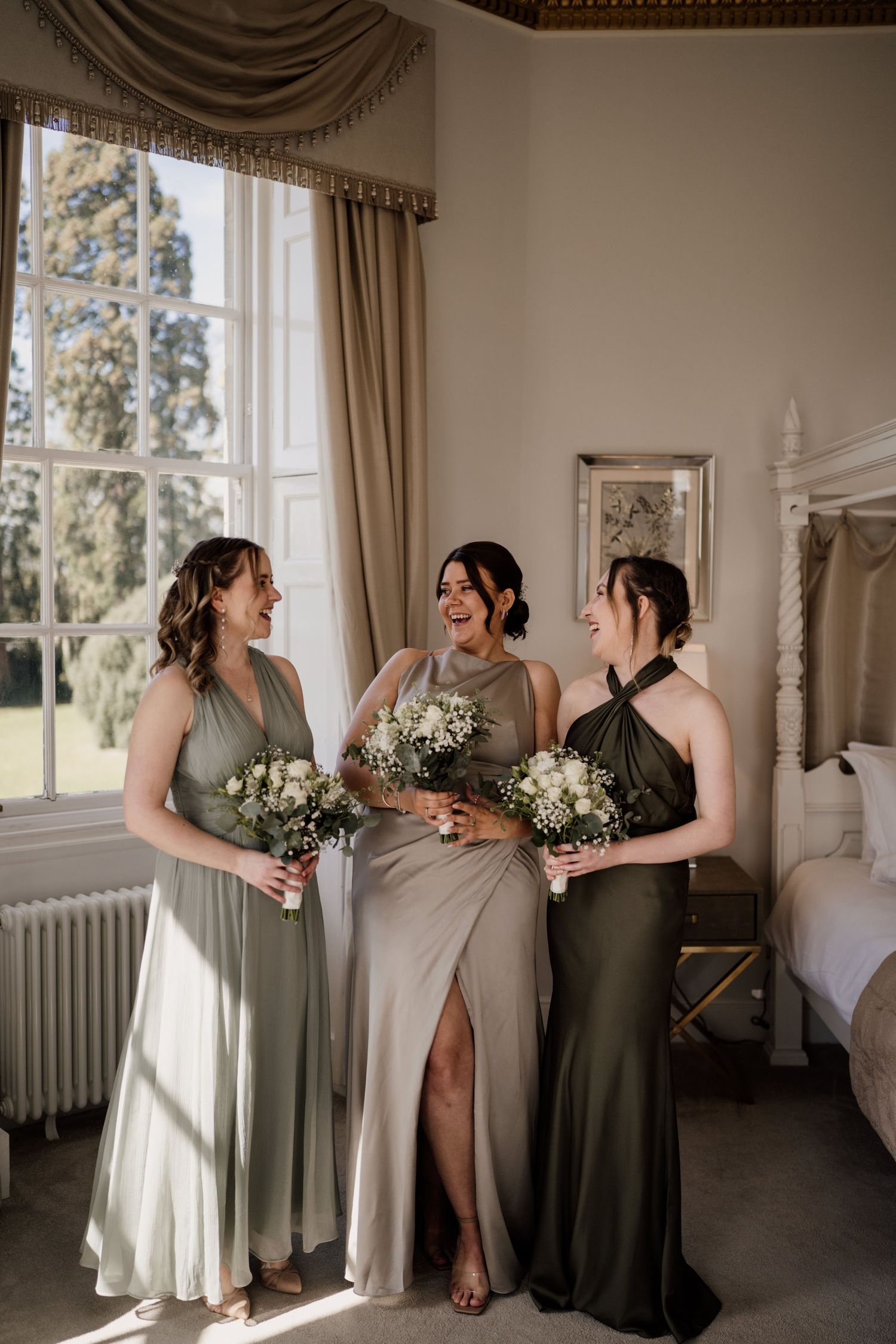 Bridesmaids stood in front of a window laughing at each other.